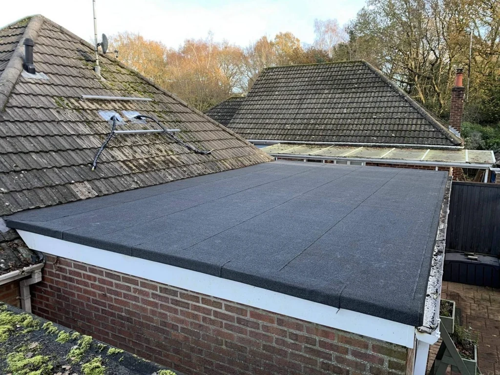 Dark felt garage roof with white fascia above a brick wall